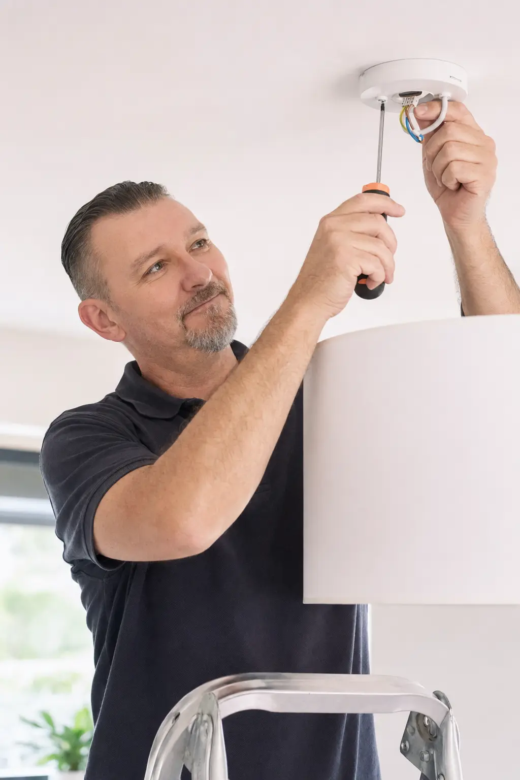 Artisan installant un plafonnier sur un escabeau à Nancy
